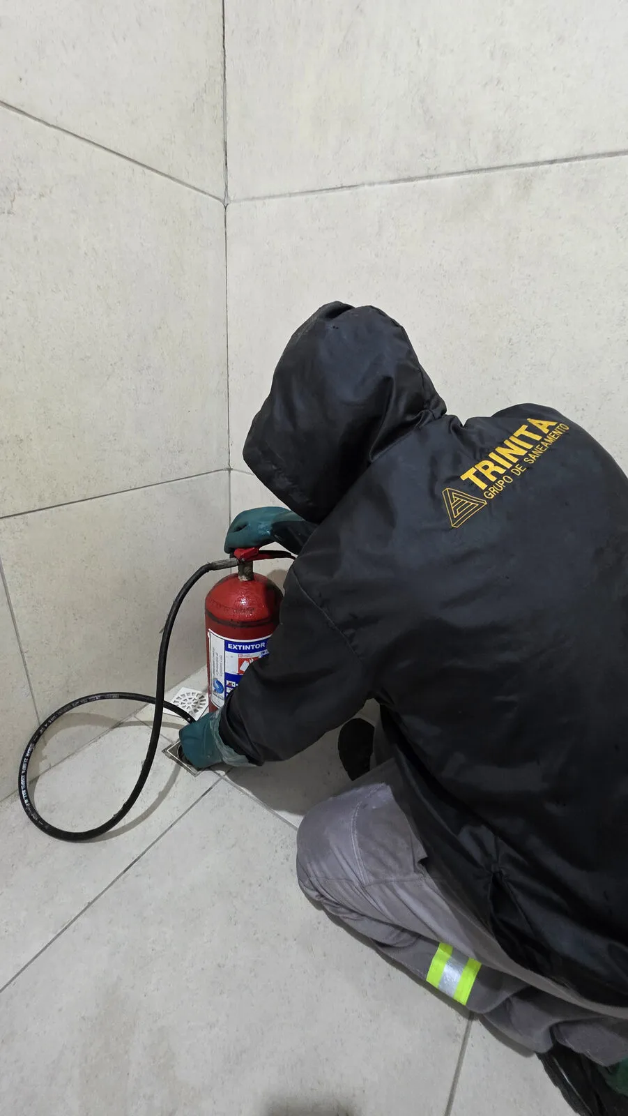 Técnico uniformizado da Trinitá desentupindo o ralo de um banheiro